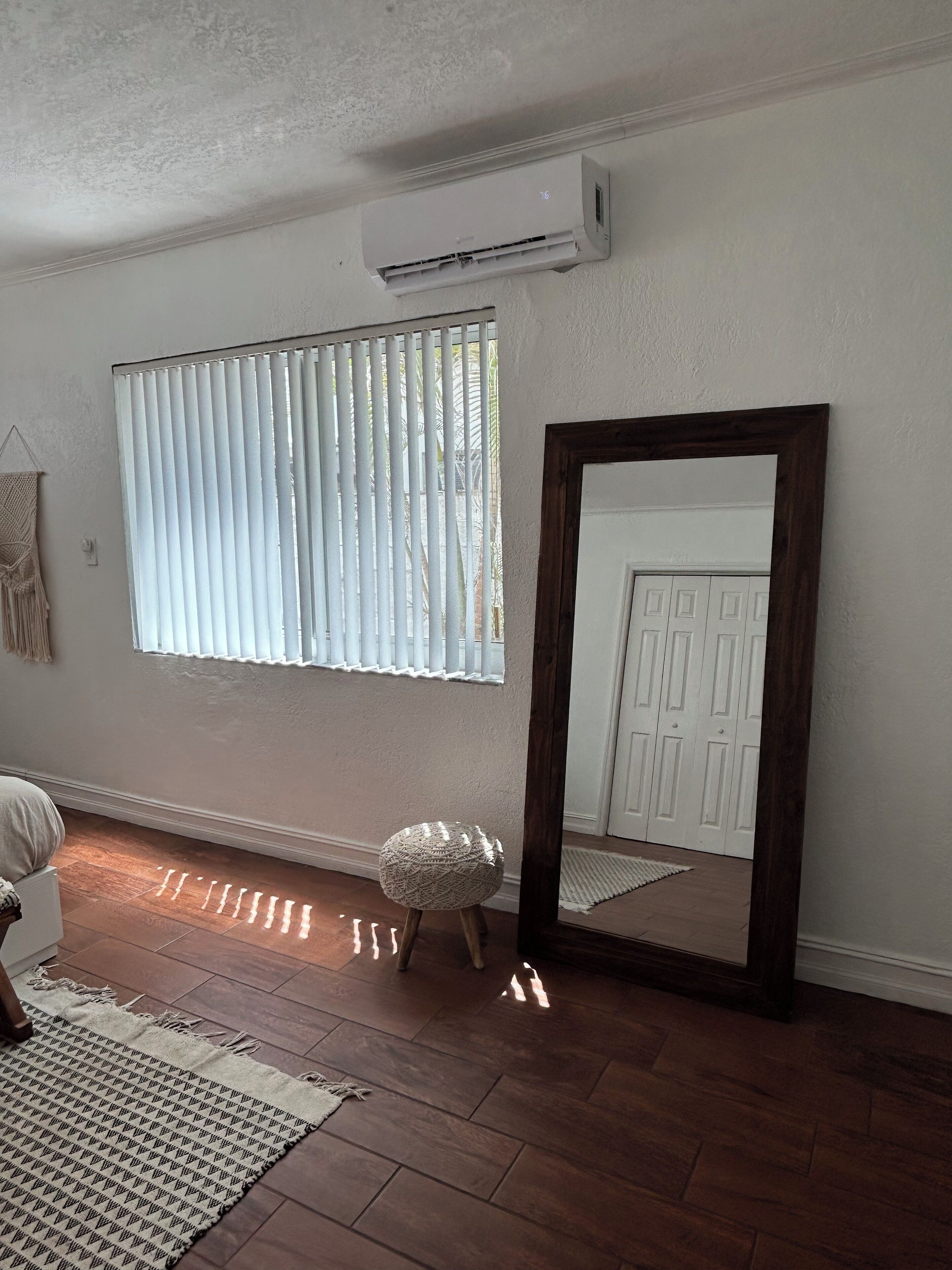 A room with a large mirror, a standing lamp, and a window with blinds.
