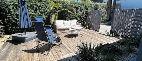 A wooden deck with outdoor furniture, including a lounge chair, a small table, and a sofa.