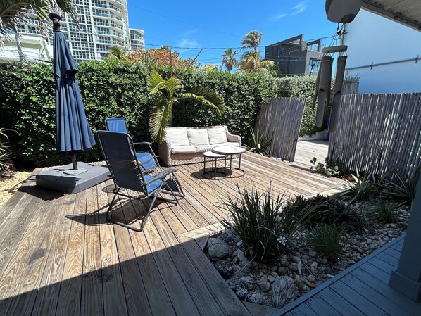 A wooden deck with outdoor furniture, including a lounge chair, a small table, and a sofa. - Walnut Beach Bungalow (Hollywood)