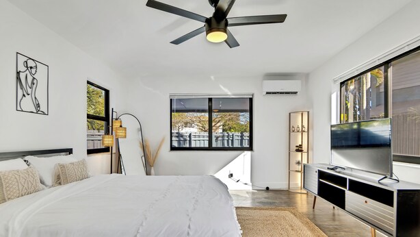 Une chambre à coucher moderne, dotée d’un grand lit, d’un ventilateur de plafond, d’une télévision et d’une fenêtre donnant sur l’extérieur.