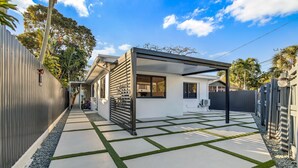 Une maison moderne dotée d’un patio couvert, d’un chemin en béton agrémenté de touches de verdure et d’une clôture en métal.
