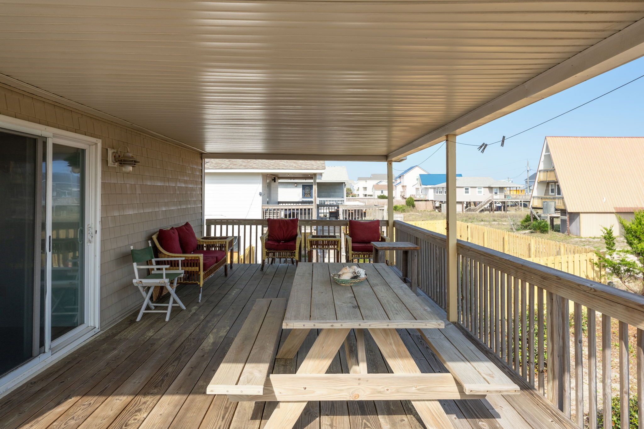 Una terraza techada al aire libre con piso de madera, una mesa con sillas y vistas a casas vecinas.