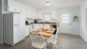 A modern kitchen with white cabinets, a wooden dining table, and a refrigerator.