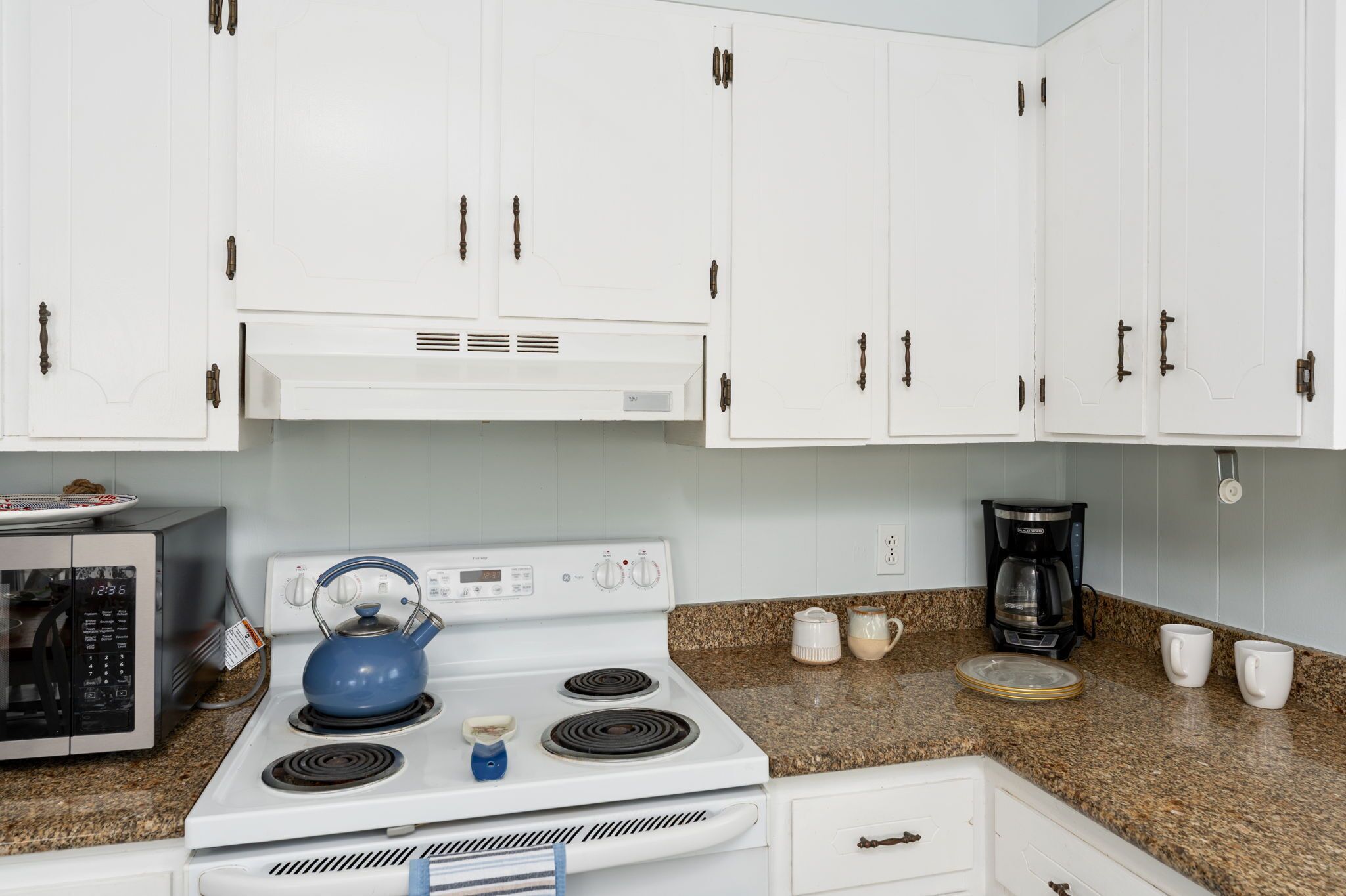 A kitchen with white cabinets, a white stove, a blue kettle, a coffee maker, and a microwave.