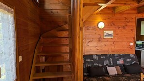 Un interior de madera con una escalera, un sofá con cojines estampados de 'URBAN' y un pequeño cuadro en la pared.