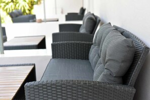 A modern outdoor seating area with a long, dark wicker sofa and matching cushions, a wooden table, and a wicker chair. - LiRi - Family paradise (Ialysos)