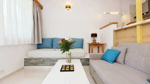 A living room with a sofa, a coffee table with a vase and cookies, and a bed with blue pillows. - LiRi - Family paradise (Ialysos)