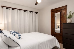 Une chambre à coucher comprenant un lit, une table de chevet, une commode, un miroir et un ventilateur de plafond.