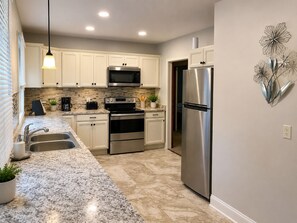 A modern kitchen with white cabinets, stainless steel appliances, a granite countertop, and a decorative wall piece. - The Evergreen - Hear the Roar of Niagara Falls - 5 Minutes to Niagara Falls (Niagara Falls)