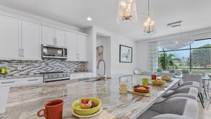 A modern kitchen with white cabinets, a stainless steel microwave, and a large island with seating.