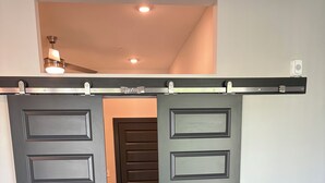 A modern interior with a sliding door leading to another room, a dark-colored sofa, and a ceiling fan. - Cozy Luxury Unit Convenient location (Decatur)