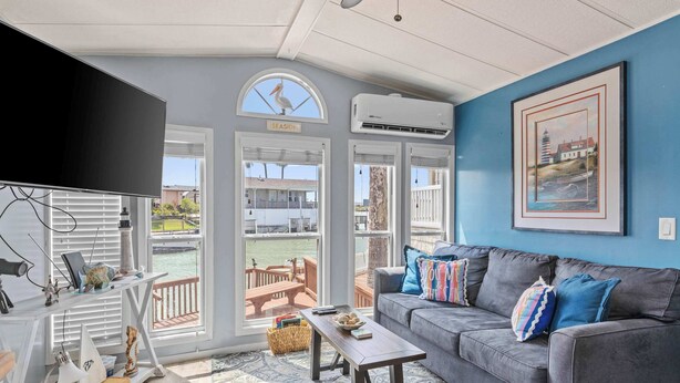 A living room with a grey sofa, a coffee table, a TV, and a view of the sea.