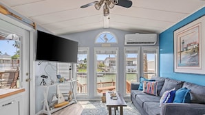A living room with a gray sofa, a television, a ceiling fan, and a view of the water.