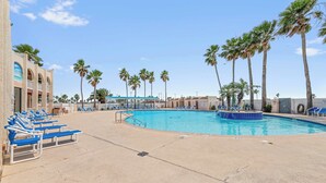 A pool area with blue lounge chairs, palm trees, and a building with arched windows.