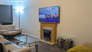 Un salon moderne doté d’un téléviseur à écran plat fixé au-dessus d’une cheminée, de canapés en cuir, d’une table basse en verre et d’un style de décoration minimaliste.