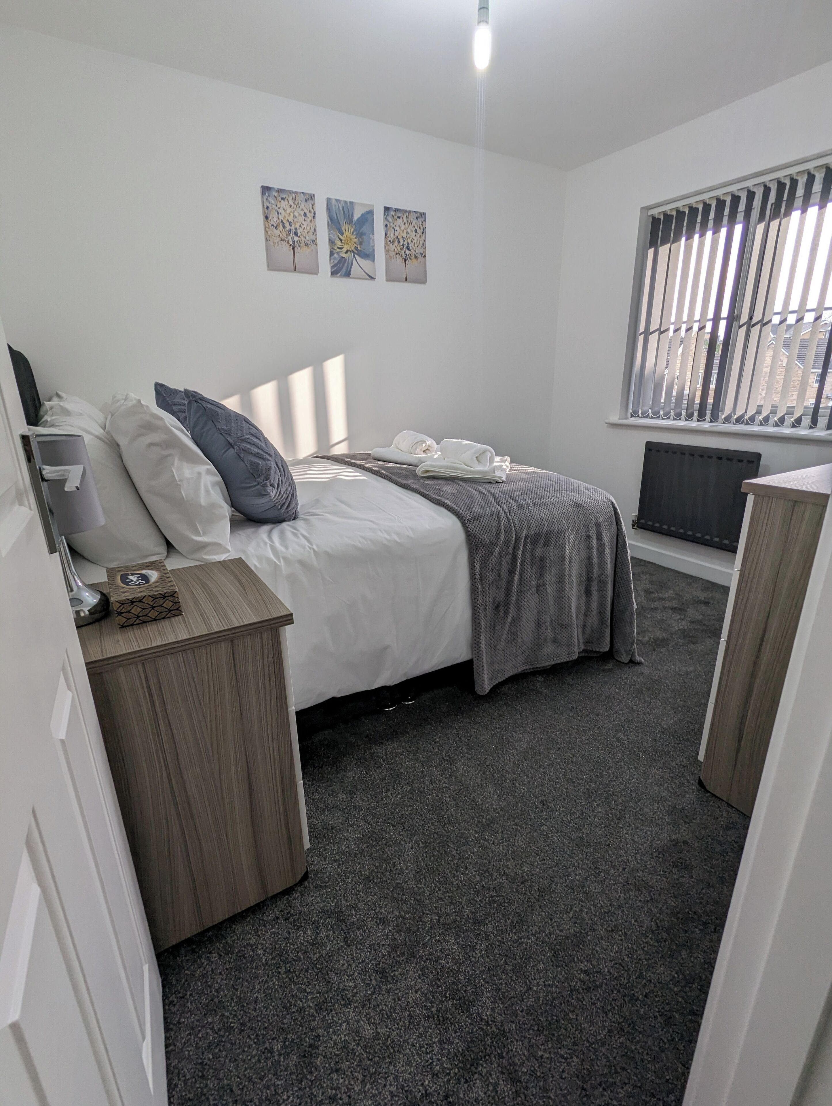 A bedroom with a bed, bedside tables, a radiator, and a window with blinds.
