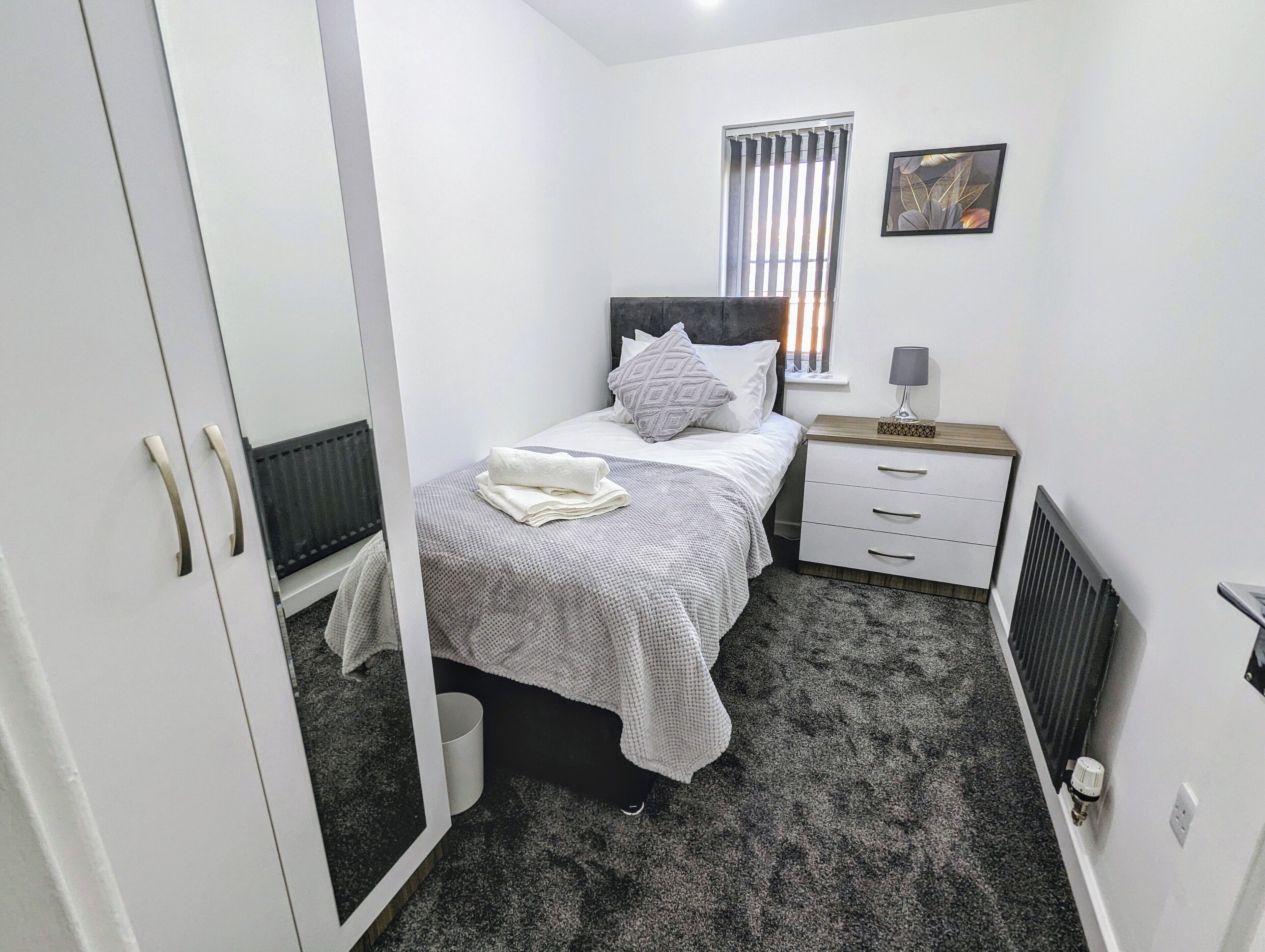 A bedroom with a bed, bedside table, and a window with blinds.
