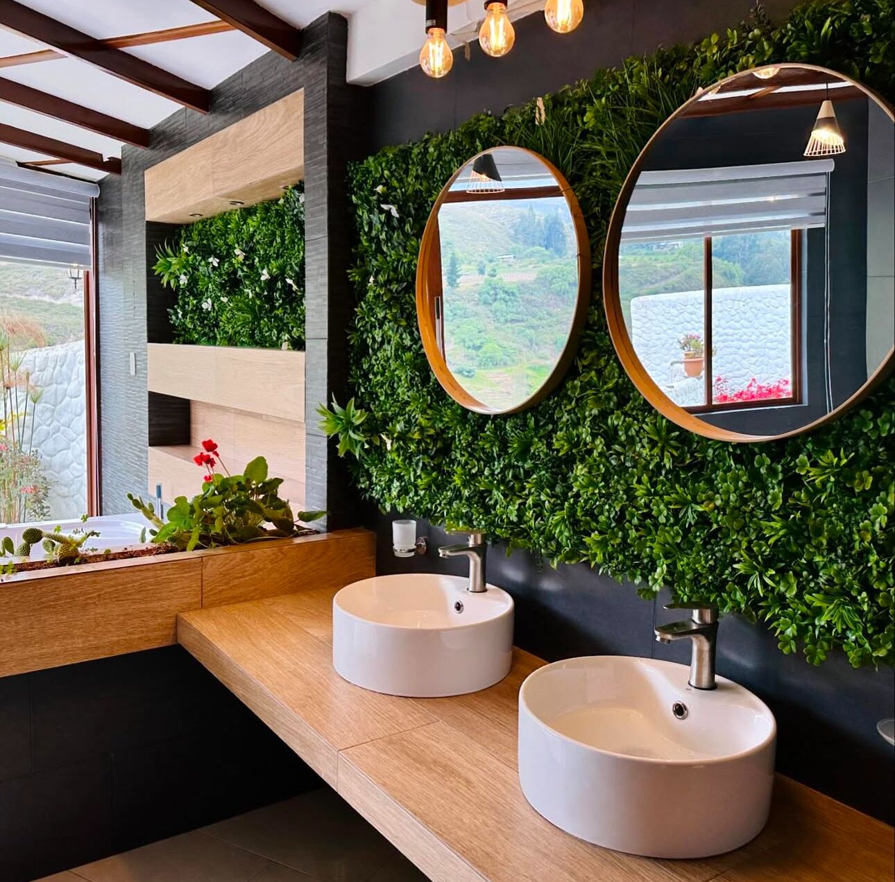 Un baño moderno con dos lavamanos redondos, un mueble de tocador de madera, una pared verde con plantas y un espejo grande.