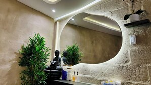 A bathroom with a large mirror, green plants, a Buddha statue, and toiletries on the counter. - Hosteria & Spa Surillal (San Miguel de Salcedo)