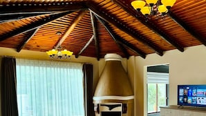 A spacious room with a large bed, a wooden ceiling, a large window with curtains, a television, and a cabinet. - Hosteria & Spa Surillal (San Miguel de Salcedo)