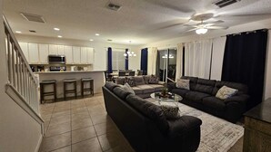 A modern living room with a large sectional sofa, a coffee table, and a dining area with a kitchen in the background. - Steps away from Resort Pool, Kids Water Park, Hot tub and Gym (Kissimmee)