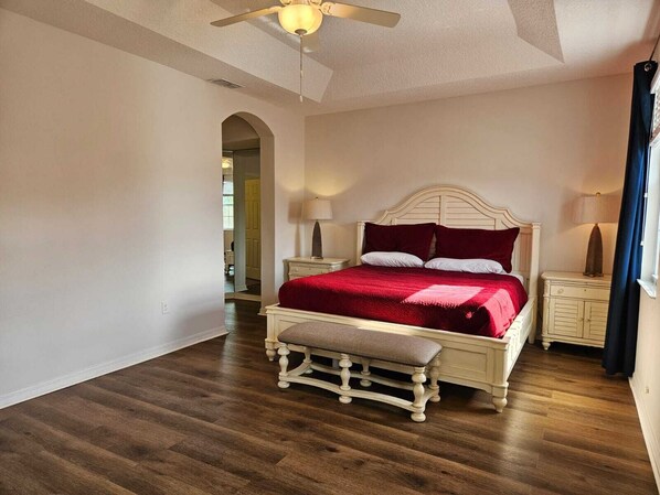 A bedroom with a large bed, a bench, two bedside tables, and a ceiling fan. - Steps away from Resort Pool, Kids Water Park, Hot tub and Gym (Kissimmee)