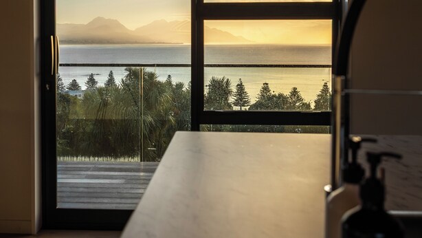 Una habitación con un amplio ventanal corredera que da a un balcón con vistas a un cuerpo de agua y montañas.