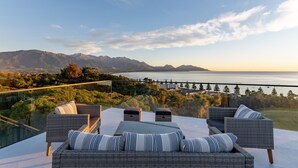 Una terraza con mobiliario de mimbre y vistas a montañas y un cuerpo de agua.