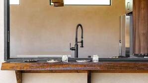 Una cocina moderna con un ventanal grande, una lámpara colgante y cuatro taburetes de madera.