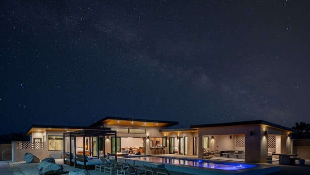 Una casa moderna con piscina, ventanas amplias y un cielo nocturno estrellado.