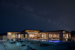 A modern house with a swimming pool, large windows, and a starry night sky.