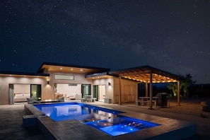 A modern house with a swimming pool, outdoor seating, and a covered patio area.