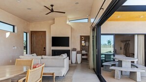 Una sala de estar moderna con un sofá, una mesa de comedor y sillas, una chimenea y un ventanal grande.