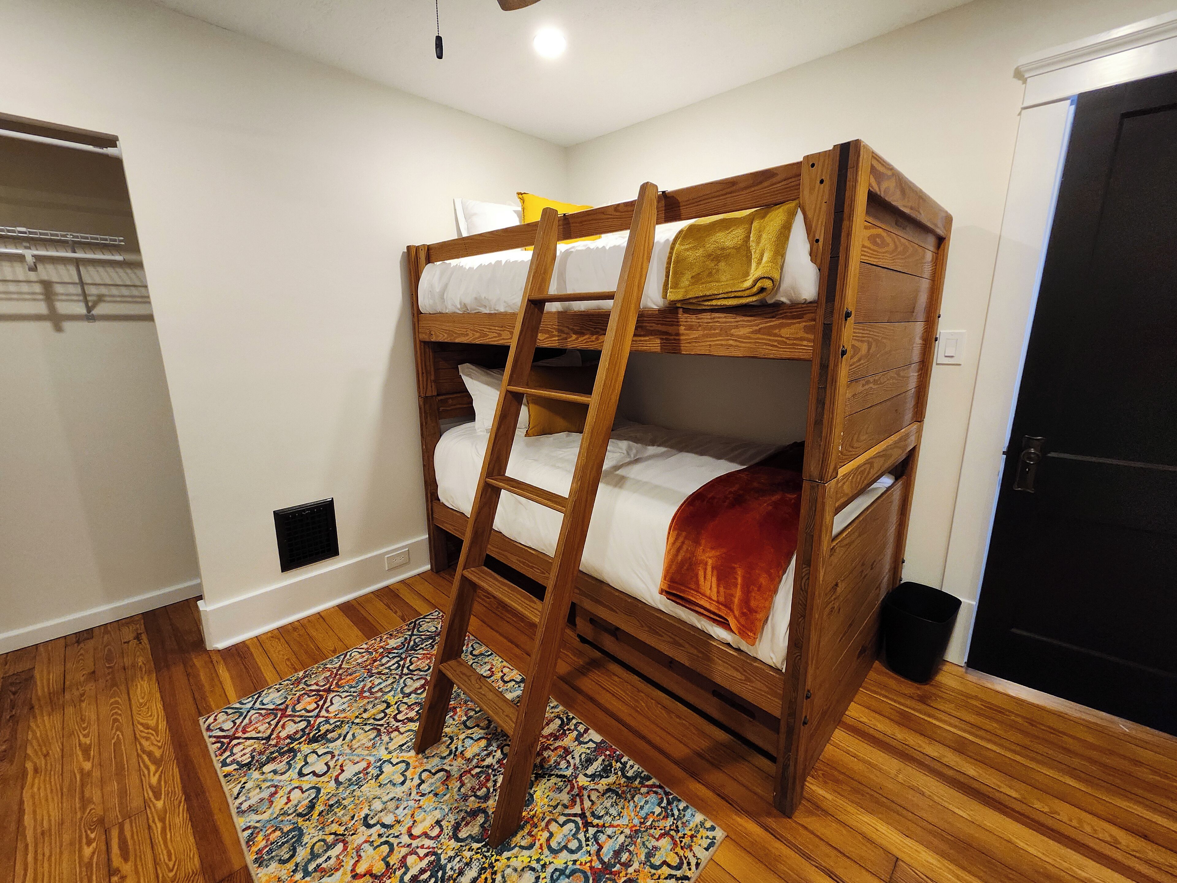 A bunk bed with a ladder, a patterned rug, and a door in a room with wooden flooring.