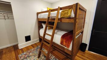 A bunk bed with a ladder, a patterned rug, and a door in a room with wooden flooring.