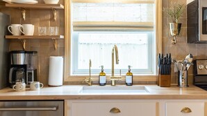 Eine Küche mit großem Fenster, einer Kaffeemaschine, einem Spülbecken mit goldenen Wasserhähnen und einem Messerblock.