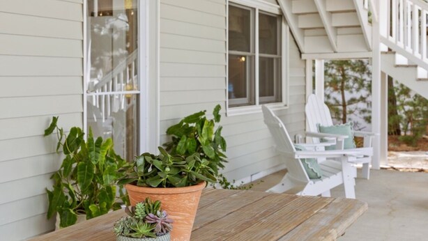 Eine Veranda mit einem Holztisch, Blumentöpfen und weißen Gartenmöbeln.