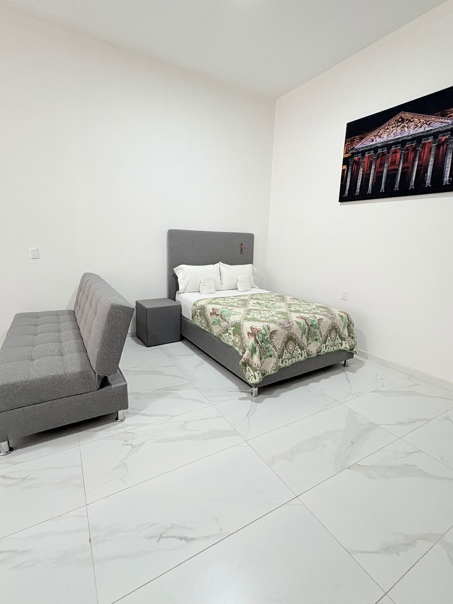 A bedroom with a bed, a grey sofa, and a small bedside table.