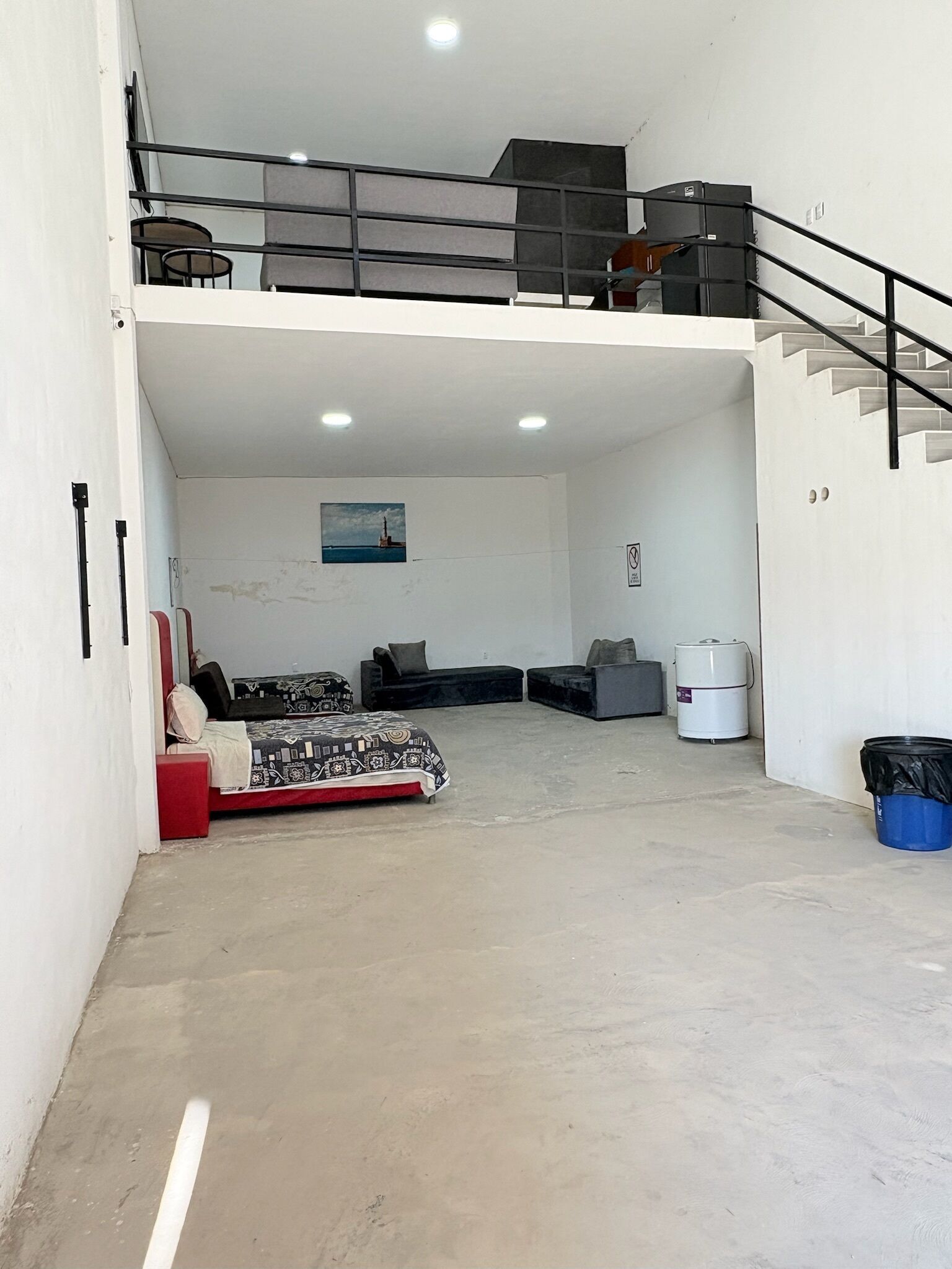 A spacious living area with a high ceiling, a staircase, and a view of the sea.