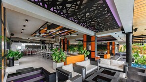 Un salon intérieur moderne, doté de meubles en osier, d’un bar et offrant une vue sur la piscine.