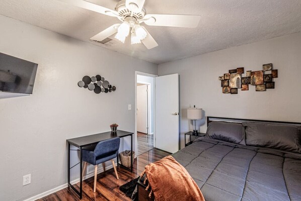 Une chambre à coucher comprenant un lit, un bureau avec une chaise, un ventilateur de plafond et des œuvres d’art murales.