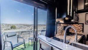 Een balkon met uitzicht over een woestijnlandschap, een keuken met een marmeren aanrecht, en een zithoek met twee stoelen.