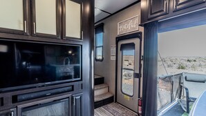 Een compact RV-interieur met een televisie, een zithoekje en een deur naar buiten.