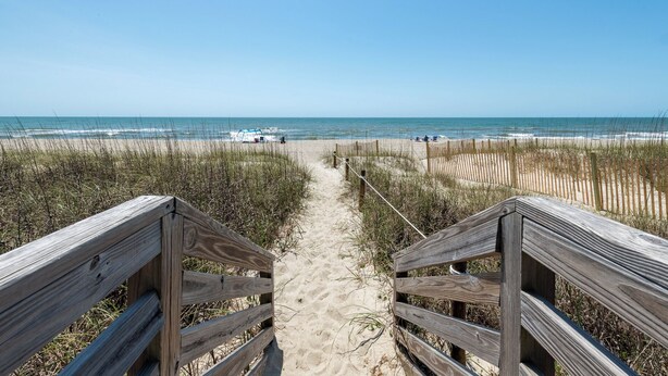 A wooden boardwalk leading to a beach with a clear view of the ocean.