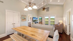 A spacious living area with a wooden dining table, a ceiling fan, and a view of a golf course through large windows.
