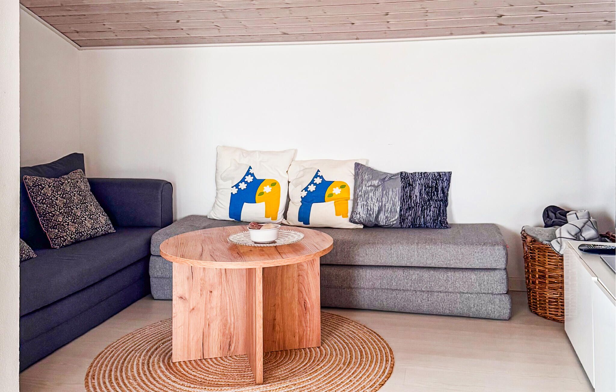 Ein Wohnzimmer mit grauem Sofa, rundem Holztisch und gemusterten Kissen.