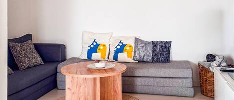 Ein Wohnzimmer mit grauem Sofa, rundem Holztisch und gemusterten Kissen.