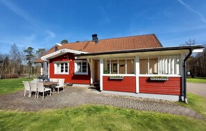 A red building with a tiled roof, a covered outdoor seating area, and a paved patio. - Nice home in Vittsjö with sauna (Vittsjö)
