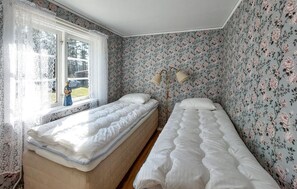 A bedroom with two single beds, floral wallpaper, a window with lace curtains, and a floor lamp. - Nice home in Vittsjö with sauna (Vittsjö)