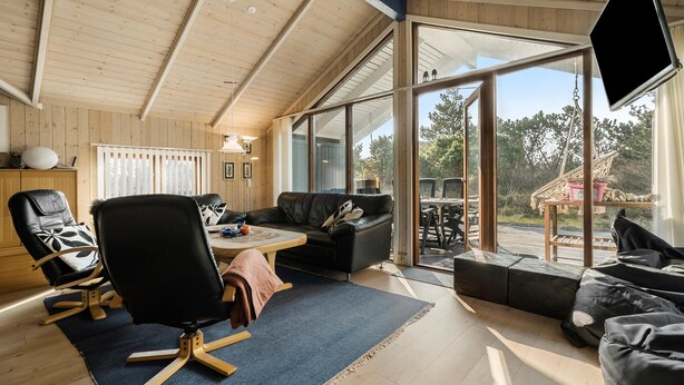 A spacious living area with a wooden ceiling, a large TV, and a view of the outdoors. - Lovely home in Ringkøbing with sauna (Ringkøbing)